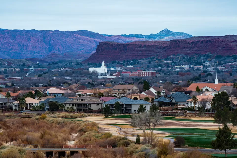 Town of St. George, Utah with small white church and red rock cliffs in background